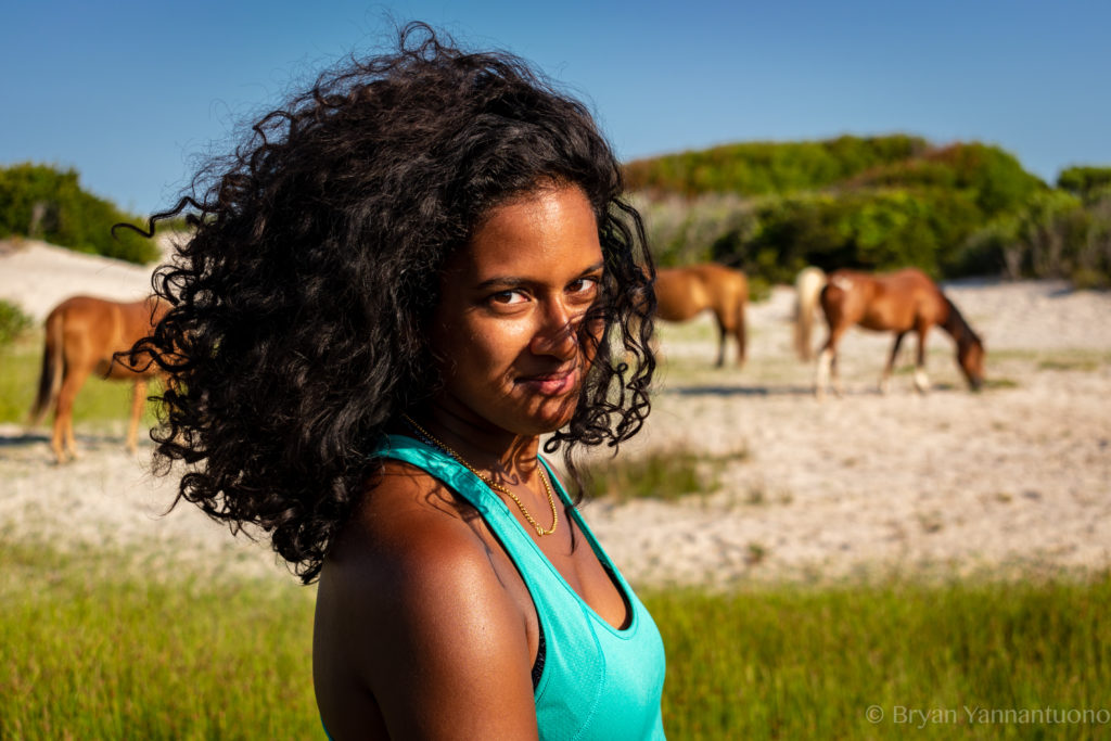 A beautiful young woman looks mysteriously at the camera in front of three wild horses. As a photographer in DC, I specialize in showcasing my clients' personalities