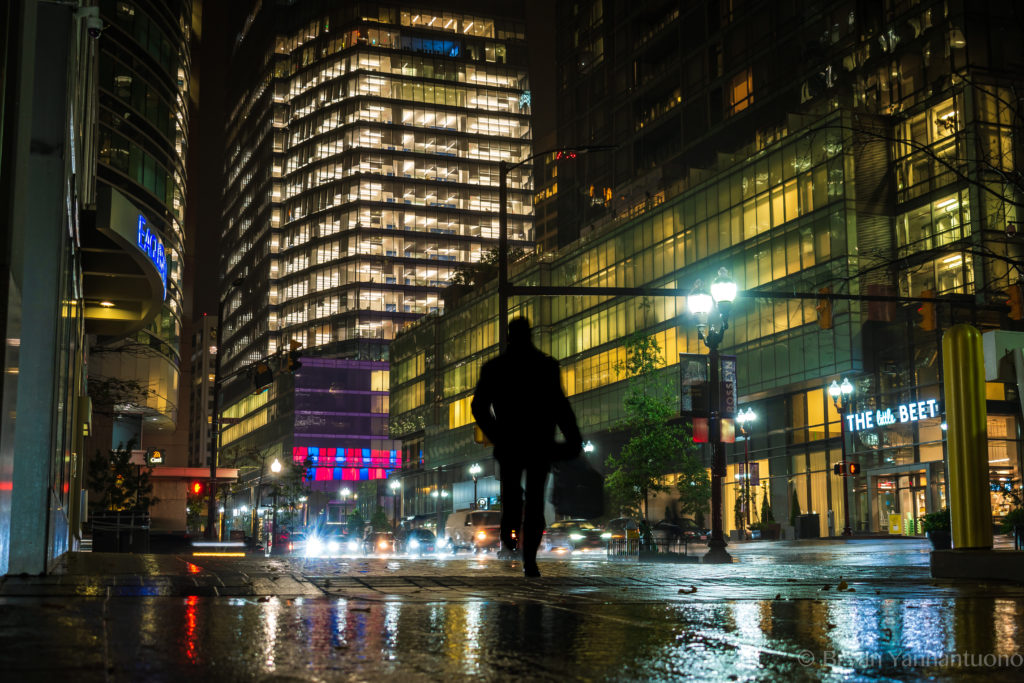 Street photography - A silhouette of a man walking in a major rainstorm at night against the neon lights of Rosslyn, Virginia