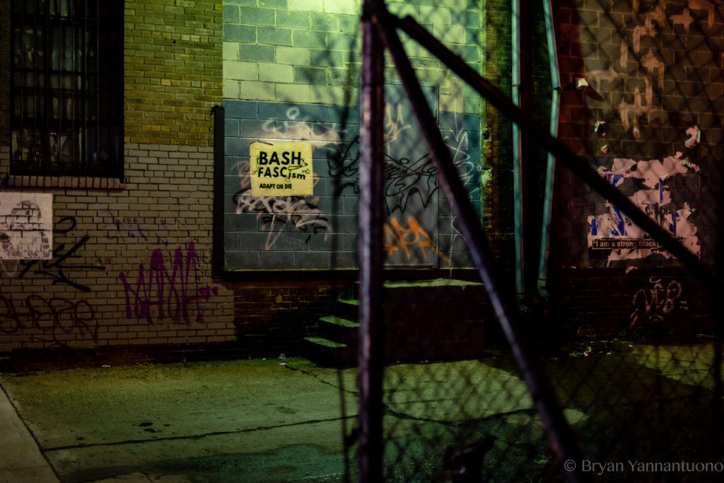 Street photography - An eery street scene of a barbed wire fence, graffiti, and a sign that reads "Bash Fascism"