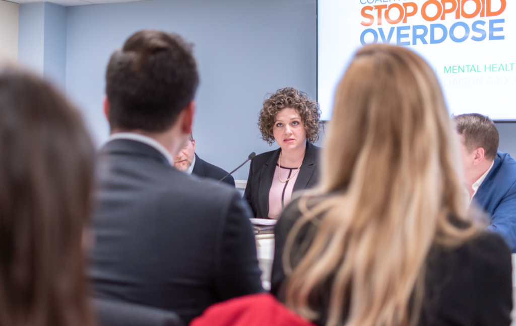 A professional woman leads a panel as the crowd listens