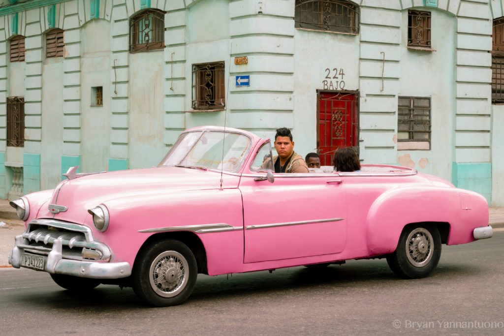 Travel photography of Cuban men cruising Havana in a bright pink convertible