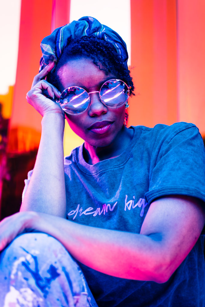 The photograph is of a young woman poses with neon purple sunglasses