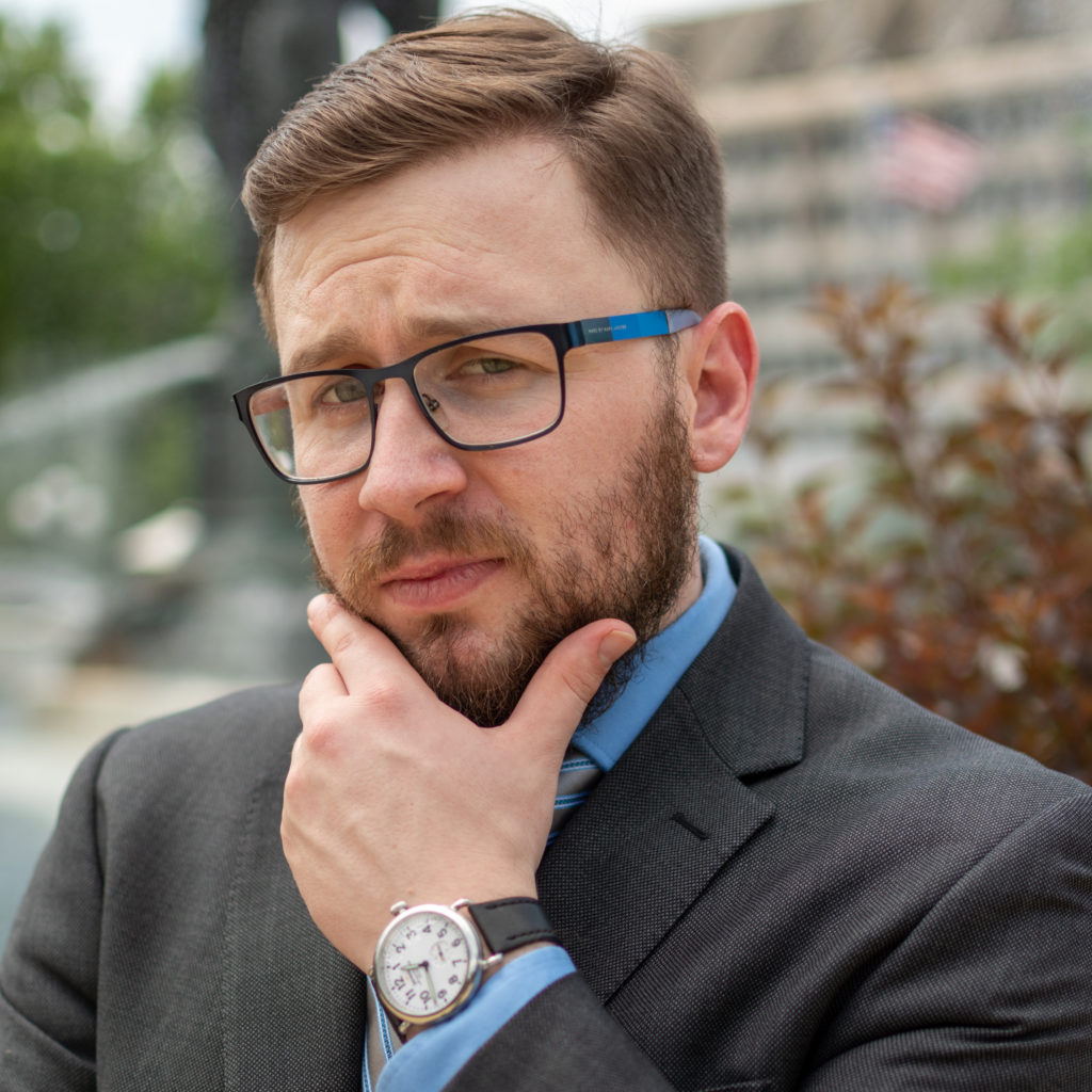 A man dressed in a suit poses for a professional headshot