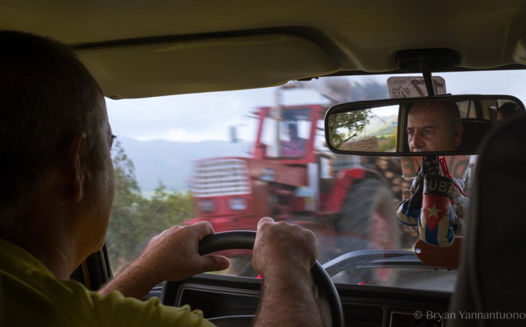 A cuban taxi triver looks in the rearview mirror as a red tractor passes