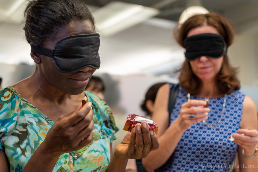 Two blindfolded woman sample mystery flavors of candy at an event