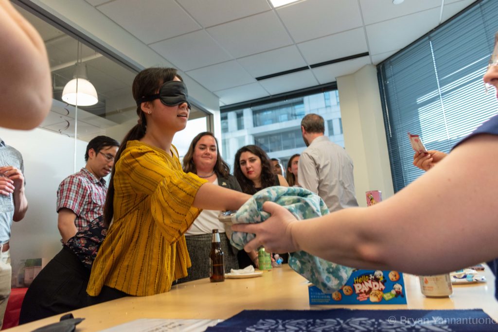 A blindfolded woman reaches into a mystery box