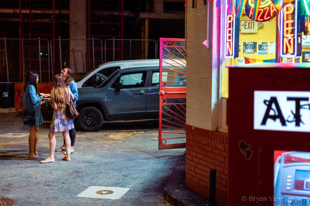 Street photography - A street scene of three young woman eat jumbo slice pizza in the parking lot of a bright neon restaurant on U Street neighborhood of Washington, DC